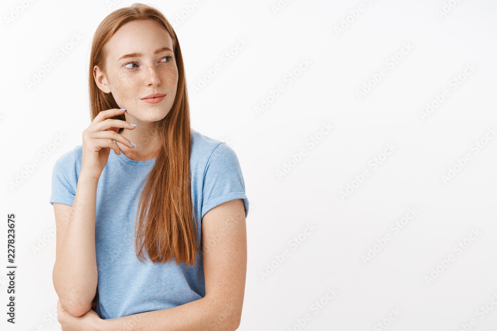 Waist-up shot of flirty intrigued and interested good-looking adult redhead female with freckles in blue t-shirt turning right with slight sensual smile and squinting looking with desire and affection Waist-up shot of flirty intrigued and interested good-looking adult redhead female with freckles in blue t-shirt turning right with slight sensual smile and squinting looking with desire and affection