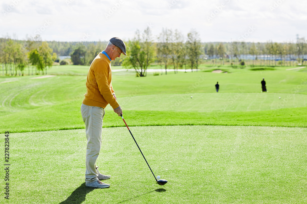 Fototapeta premium Senior man in casualwear standing in the middle of green field and going to hit golf ball