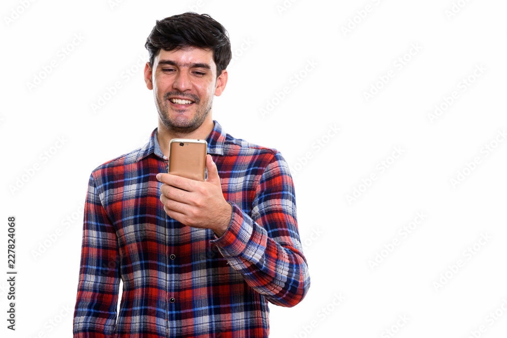 Studio shot of young happy Persian man smiling while using mobil Studio shot of young happy Persian man smiling while using mobil