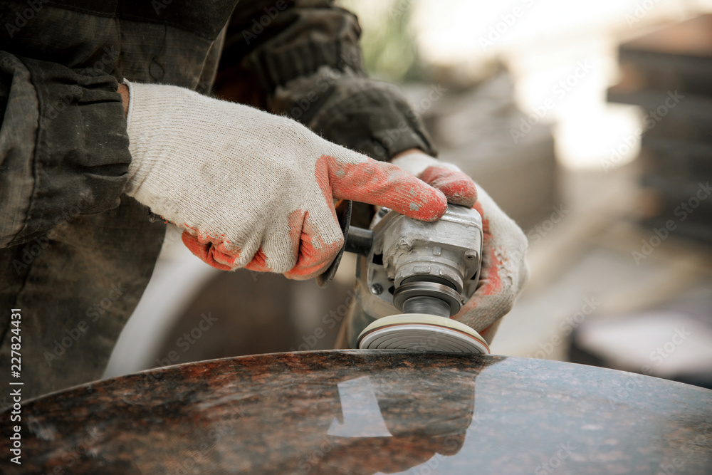 close-up a man in gloves polishes a marble monument with an angle grinder. man with a tool. worker makes a monument