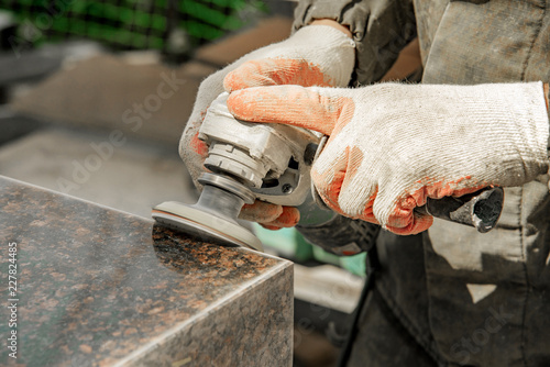 a man in work clothes and gloves polishes a marble stone with an angle grinder. grinding stone. manufacturing of monuments. marble slab photo