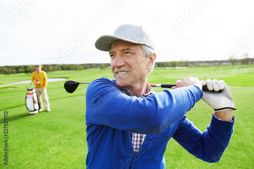 Mature grey-haired man with golf club behind back hit the ball during outdoor game
