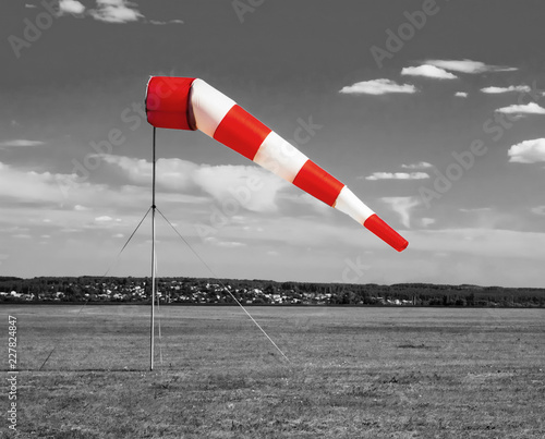 Red and white windsock wind sock on the aerodrome, monochrome black and white field, sky and clouds background