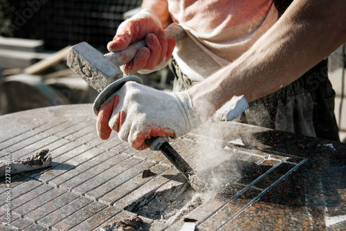 Canvas Print Stone carver in gloves working with a hammer and chisel on a marble slab