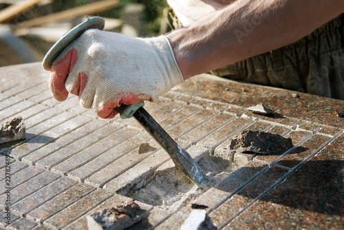close-up stone-cutter in gloves working with a hammer and chisel on a marble slab. a man in work clothes in the dust. painstaking work