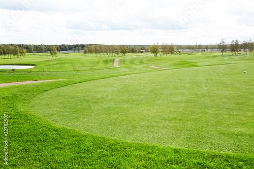Vast green field for playing outdoor games such as golf and riverside surrounded by trees on background © pressmaster