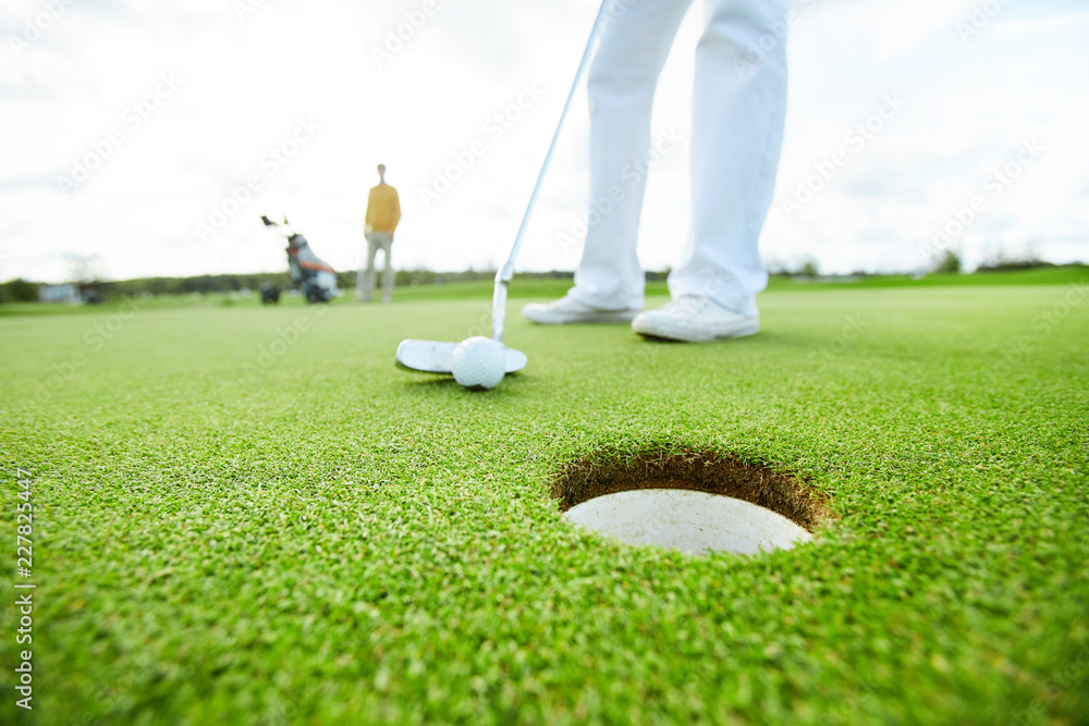 Obraz premium Golf player holding club close to the ball before hitting it while targeting at hole