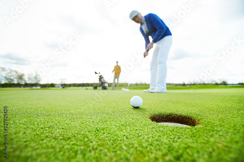 Golf ball close to hole in the ground on background of golf player going to hit it