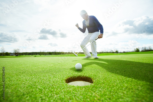 Active man hitting golf ball while standing on green field and looking after it