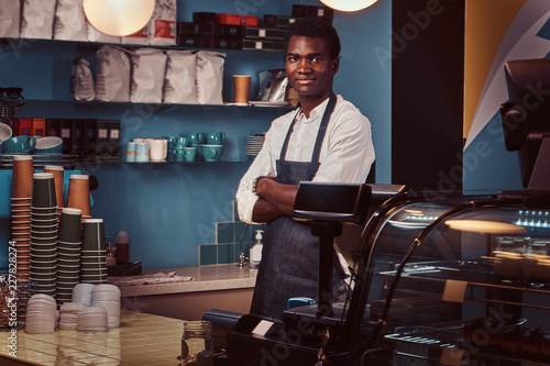 Portrait of a handsome African barista at counter of a trendy coffee shop.