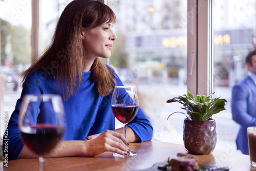 Beautiful woman drinking red wine in cafe near window. lady watches into window at the guy in blue suit.