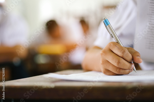 Close-up of writing hands of uniform students taking exam at course.