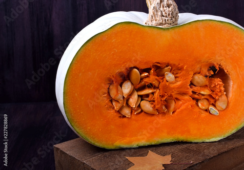 Fotografie Half of a pumpkin with orange flesh on a wooden board surrounded by dry maple le