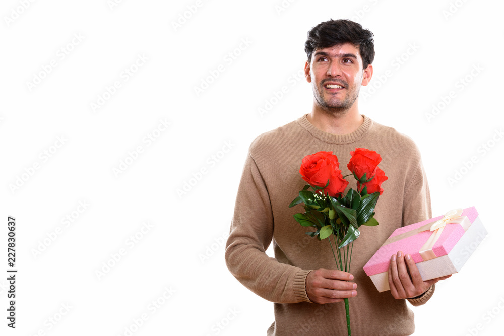 Thoughtful young happy Persian man smiling while holding red ros Thoughtful young happy Persian man smiling while holding red ros
