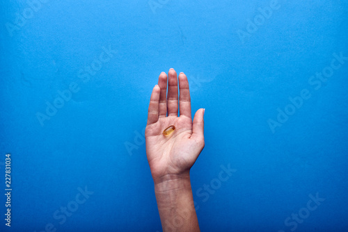 A woman holds a transparent fish oil capsule, a useful source of omega-3. Treatment with dietary supplements, vitamins and minerals. Pharmaceutical advertising in the style of minimalism.
