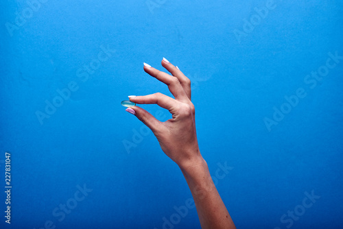 A woman holds a transparent fish oil capsule, a useful source of omega-3. Treatment with dietary supplements, vitamins and minerals. Pharmaceutical advertising in the style of minimalism.