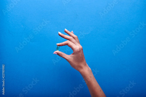 A woman holds a transparent fish oil capsule, a useful source of omega-3. Treatment with dietary supplements, vitamins and minerals. Pharmaceutical advertising in the style of minimalism.