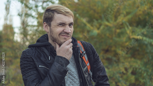 A handsome guy posing against the autumn nature. Blond in a leather jacket on the street