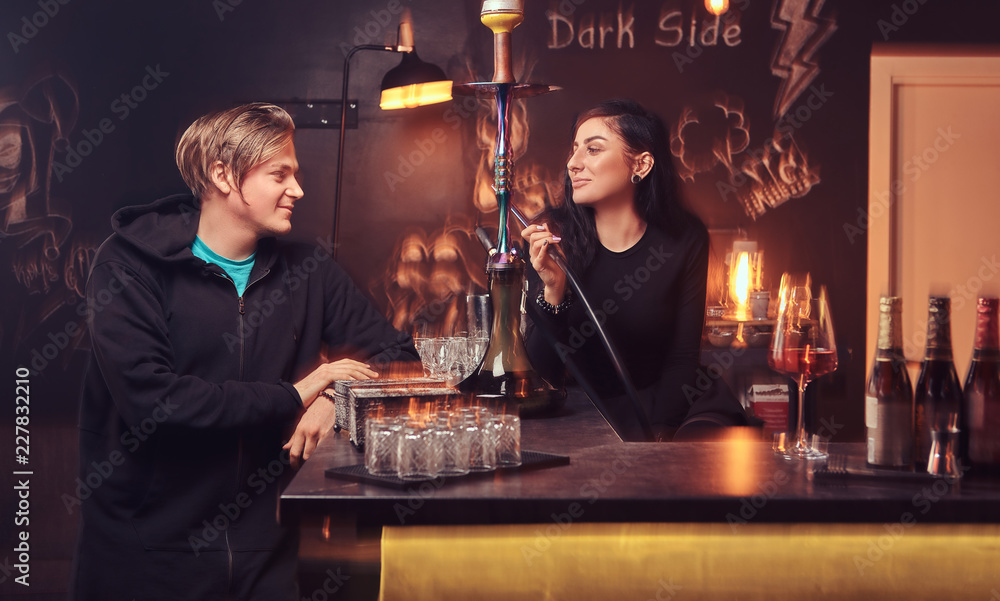 Seductive brunette womansmokes a hookah and handsome guy in hoodie. Seductive brunette womansmokes a hookah and handsome guy in hoodie.