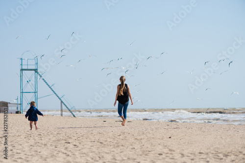 Kids walking on the sand beach with seagulls