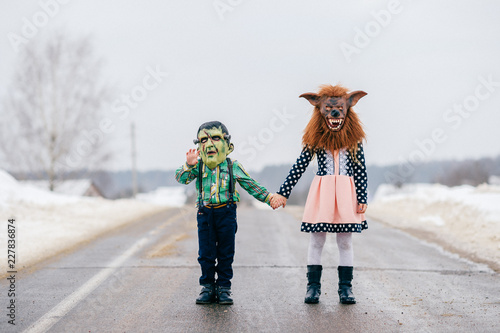 Funny helloween children in creepy horror silicon masks portrait. Little comical kids with horrible makeup celebrating halloween in winter. Countryside holidays. Frankentstenin and werewolf masks. photo