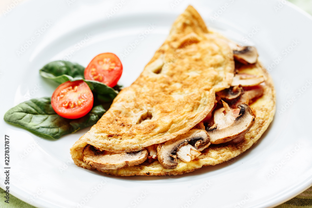 Omelet with mushrooms served on white plate with cherry tomatoes and spinach Omelet with mushrooms served on white plate with cherry tomatoes and spinach