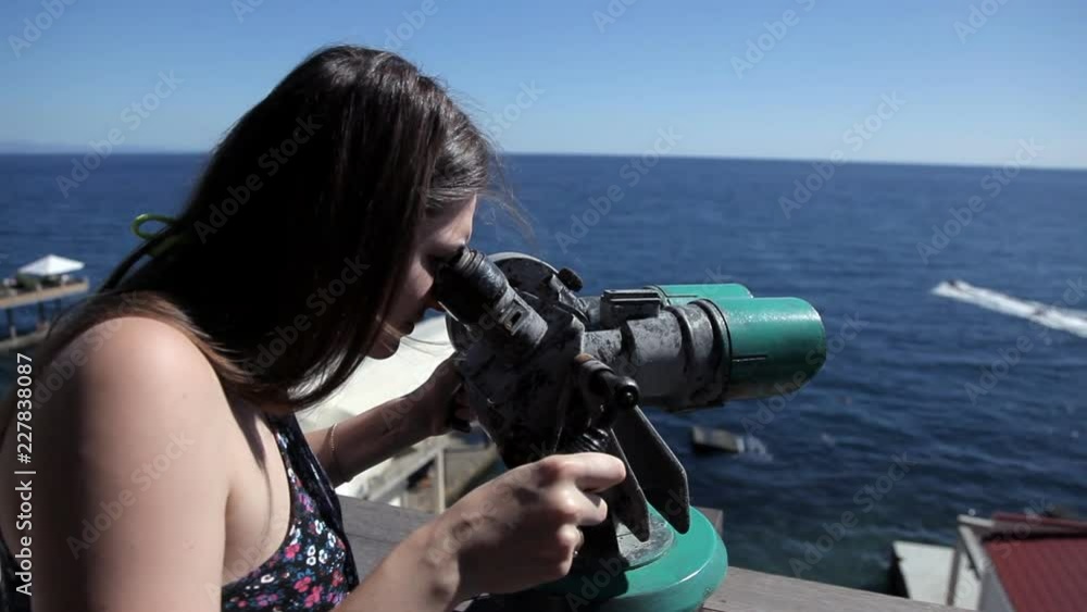 A young girl stands on the observation deck overlooking the sea and looks through a telescope A young girl stands on the observation deck overlooking the sea and looks through a telescope