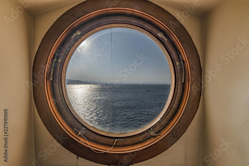 Oblò rotondo in legno con vista sul mare e barche a vela photo