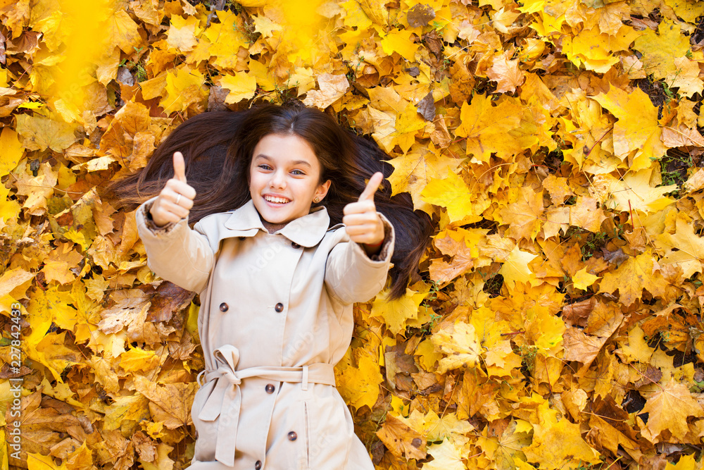 Young beautiful little girl in beige coat lying on yellow leaves Young beautiful little girl in beige coat lying on yellow leaves