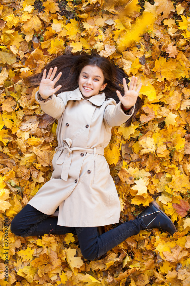 Young beautiful little girl in beige coat lying on yellow leaves Young beautiful little girl in beige coat lying on yellow leaves