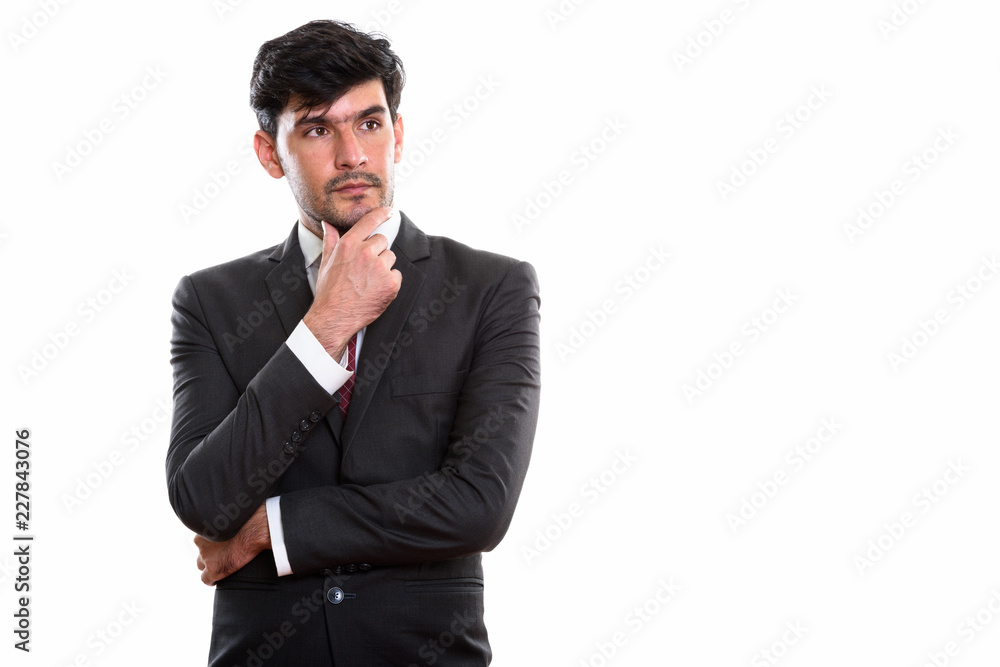 Studio shot of young Persian businessman thinking and looking at Studio shot of young Persian businessman thinking and looking at