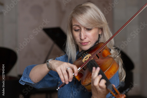 Young beautiful woman violin player looking at camera over instrument on her shoulder holding bow.