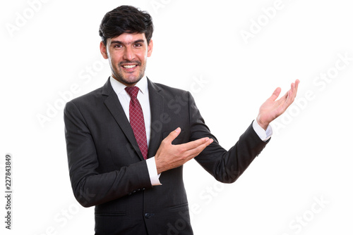 Studio shot of young happy Persian businessman smiling while sho