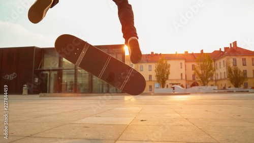 CLOSE UP: Cinematic shot of male skater landing a fakie on a sunny evening. photo