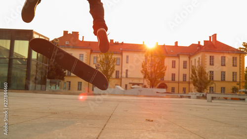 CLOSE UP: Unrecognizable skater dude does a fakie in a city square at sunset photo