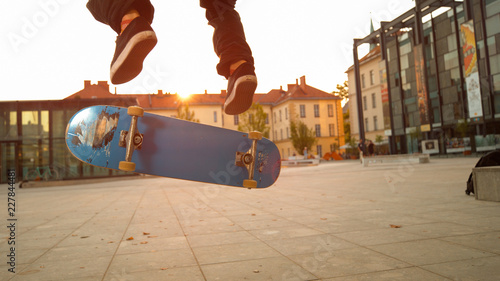 LOW ANGLE: Blue skateboard flipping underneath the young skateboarder's feet. photo