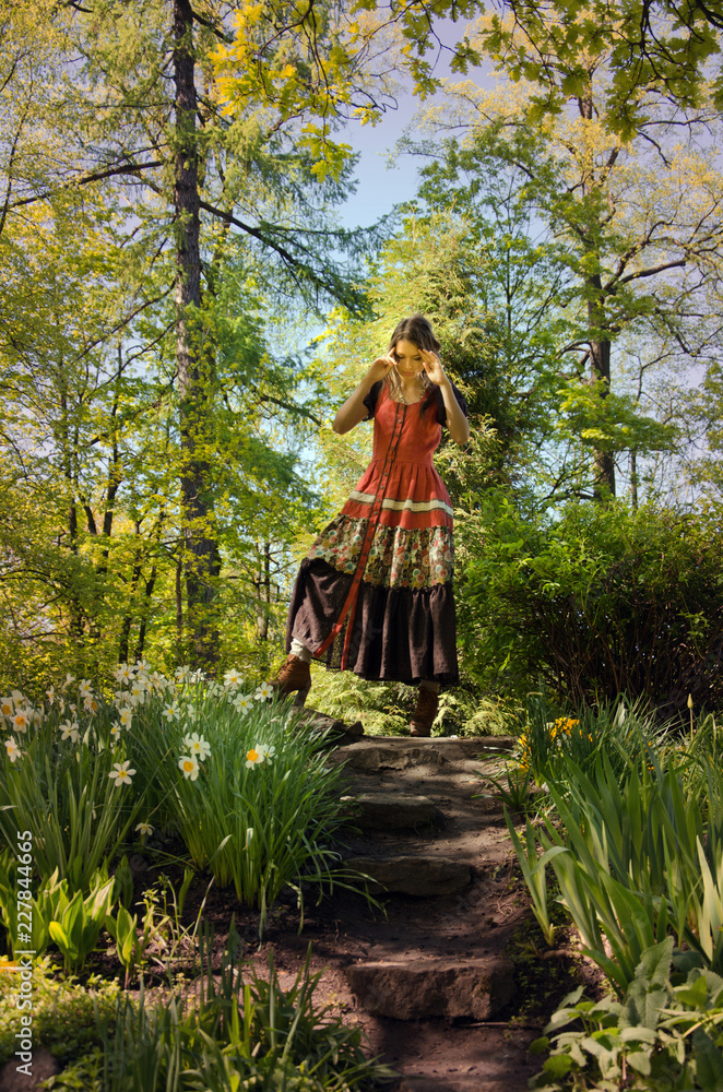 woman in a red boho style dress walks among blooming flower beds in a forest garden woman in a red boho style dress walks among blooming flower beds in a forest garden