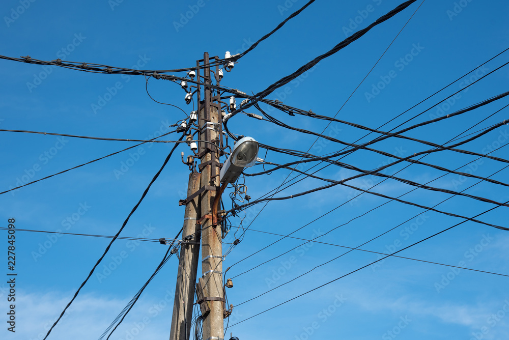 pole with electrical and telephone wires and a street lamp against a blue sky. internet cable. street lighting.