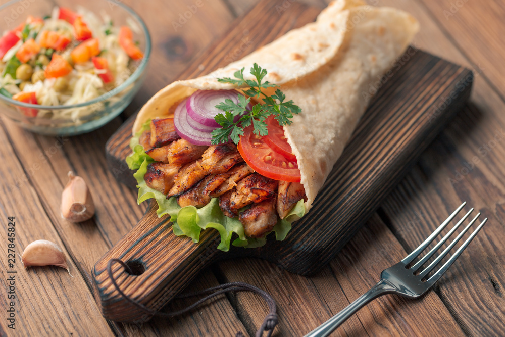 Doner kebab is lying on the cutting board. Shawarma with chicken meat, onions, salad lies on a dark old wooden table. Doner kebab is lying on the cutting board. Shawarma with chicken meat, onions, salad lies on a dark old wooden table.