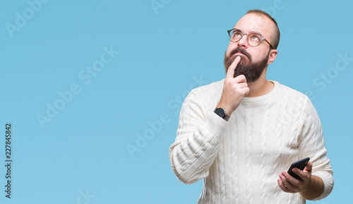 Young caucasian hipster man texting sending message using smartphone over isolated background serious face thinking about question, very confused idea
