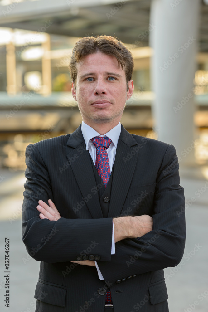 Businessman with arms crossed in front of modern building at Ban Businessman with arms crossed in front of modern building at Ban