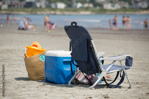 Camp chair, picnic box and a picknic basket on the beach, blurred people in backgraund