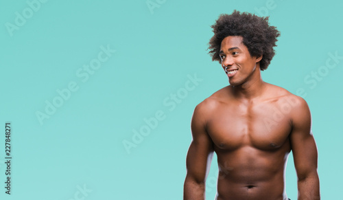 Tableau sur toile Afro american shirtless man showing nude body over isolated background looking away to side with smile on face, natural expression