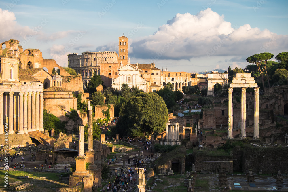 The view of Palatine and ancient Roman Forum from Capitoline Hill, with srowds of tourists walking among ruins of bildings. Collosseum is i visible in the background