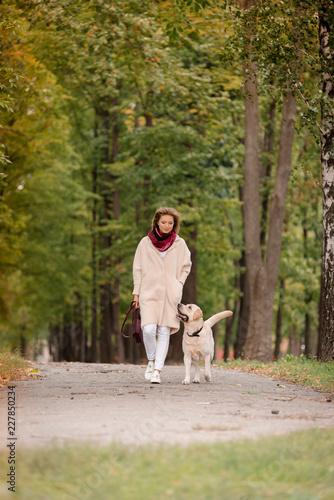 A woman walks with her labrador in the fall.