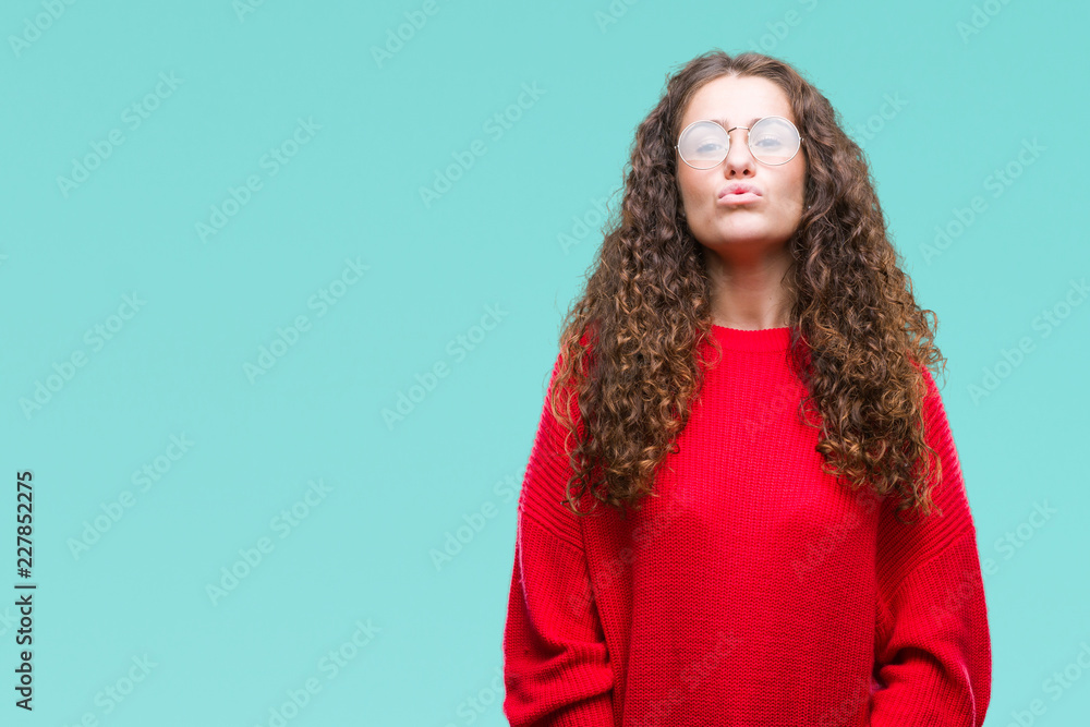 Obraz premium Beautiful brunette curly hair young girl wearing glasses and winter sweater over isolated background puffing cheeks with funny face. Mouth inflated with air, crazy expression.