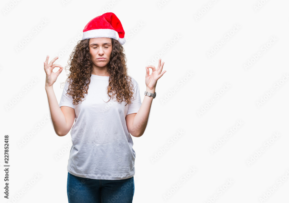 Young brunette girl wearing christmas hat over isolated background relax and smiling with eyes closed doing meditation gesture with fingers. Yoga concept. Young brunette girl wearing christmas hat over isolated background relax and smiling with eyes closed doing meditation gesture with fingers. Yoga concept.