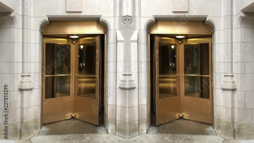 A looping shot of two golden revolving glass doors in a stone building.	