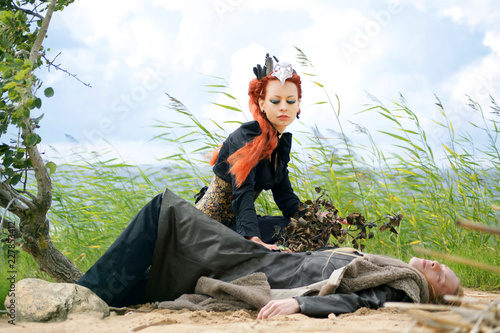 fantasy scene  redheaded fairy standing over a man s body spread out on the sand