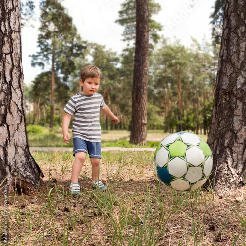 Boy kicking the ball on the play yard. Kid plays with ball in the park. Having fun outdoor. Leisure activities. Happy childhood. Healthy children concept. Outdoor activities.